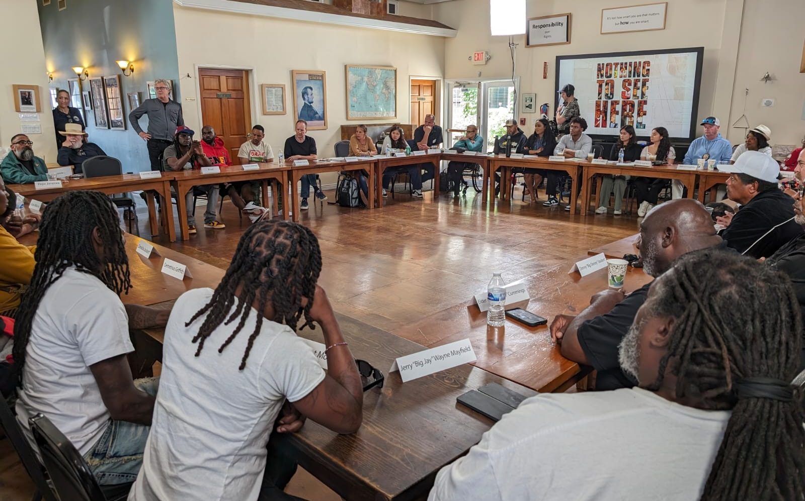 Filmmakers, gang members, police officers and victims’ families seated around a square of tables, the film’s title on the screen behind them